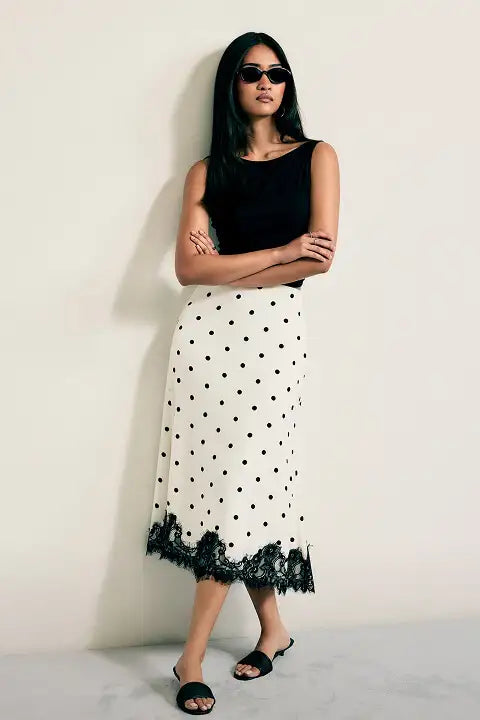 Woman wearing a black top and white polka dot skirt with lace hem against a plain background